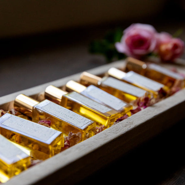 Small bottles with yellow liquid in a wooden holder on a wooden surface with flowers in the background