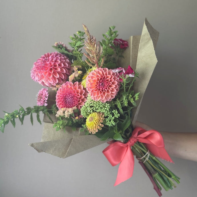 Bouquet of flowers with a pink ribbon held against a gray background