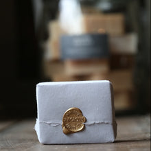 Load image into Gallery viewer, White soap bar with a gold seal on a wooden surface, with blurred background